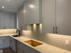 Contemporary kitchen featuring light gray cabinetry, light-toned countertops with integrated backsplash, and under-cabinet lighting - 