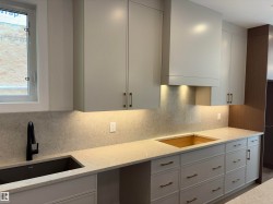Modern kitchen featuring light cabinetry with brass hardware, a dark undermount sink with a matte black faucet, and stone countertops - 