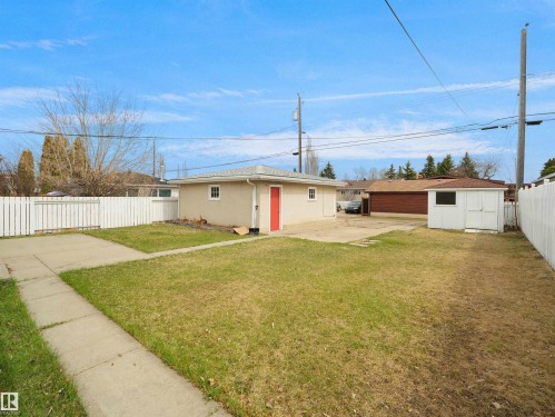 Expansive backyard featuring a detached garage with a red entry door, a separate storage shed, concrete patio space, a concrete walkway, and perimeter fencing - 8703 73 Street, Edmonton, AB - Outdoor