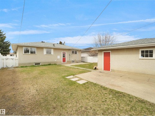 Rear exterior of the property featuring a stucco finish, multiple windows, and a red entry door - 8703 73 Street, Edmonton, AB - Outdoor