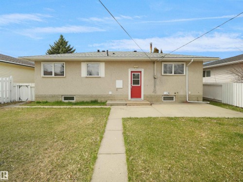 Rear exterior featuring a red entry door, stucco siding, and a concrete patio - 8703 73 Street, Edmonton, AB - Outdoor