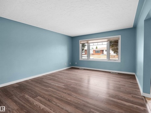 Spacious room featuring wood-finish flooring, light blue walls, and a large window with white trim - 8703 73 Street, Edmonton, AB - Indoor Photo Showing Other Room