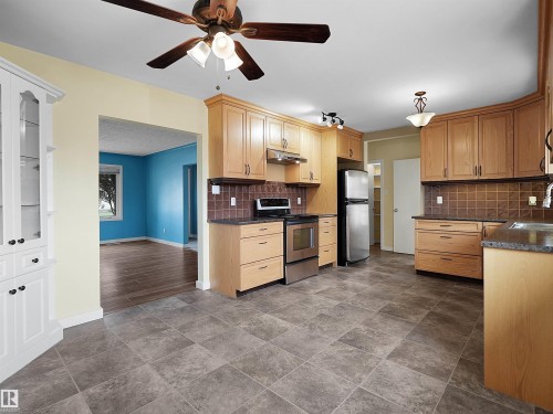 Spacious kitchen featuring light wood cabinetry, dark countertops, tiled backsplash, and stainless steel appliances - 8703 73 Street, Edmonton, AB - Indoor Photo Showing Kitchen