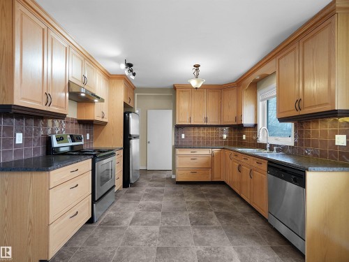 Kitchen featuring wood-finish cabinetry, dark stone-finish countertops, and a tiled backsplash - 8703 73 Street, Edmonton, AB - Indoor Photo Showing Kitchen With Double Sink