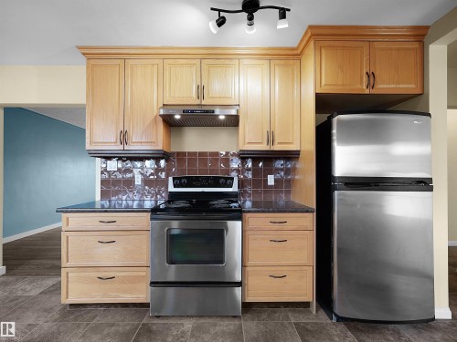 Kitchen featuring light wood cabinetry, dark speckled countertops, and a brown tiled backsplash - 8703 73 Street, Edmonton, AB - Indoor Photo Showing Kitchen