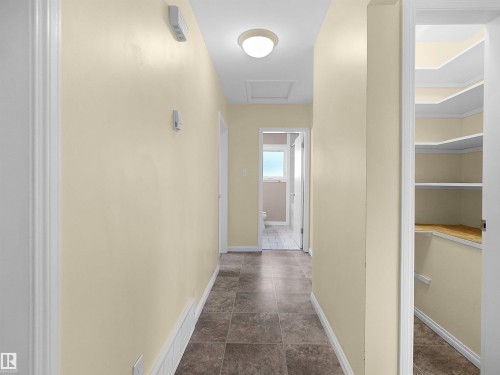 Hallway featuring neutral wall paint, tiled flooring, overhead flush-mount lighting, and an accessible storage closet with shelving - 8703 73 Street, Edmonton, AB - Indoor Photo Showing Other Room