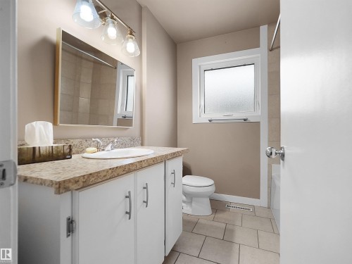 Bathroom featuring a white vanity with a patterned countertop, an integrated sink, and a framed mirror - 8703 73 Street, Edmonton, AB - Indoor Photo Showing Bathroom