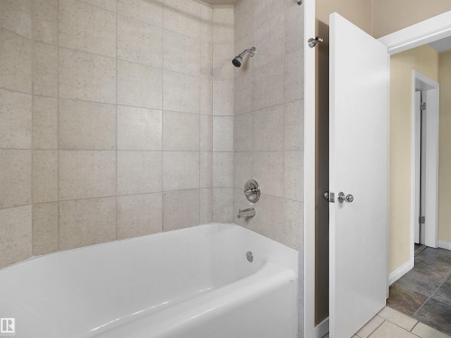 White bathtub with neutral-toned tiled surround, featuring chrome fixtures - 8703 73 Street, Edmonton, AB - Indoor Photo Showing Bathroom