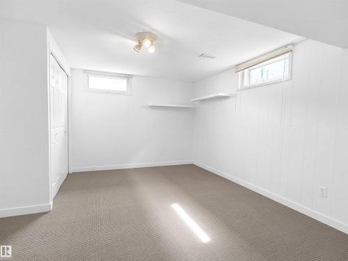 Spacious room featuring neutral carpeting, white paneled walls, two windows, and a bi-fold closet - 8703 73 Street, Edmonton, AB - Indoor