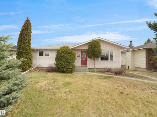 Single-story residence featuring light-colored siding, a prominent red entry door, a gabled roofline, and established front yard landscaping - 8703 73 Street, Edmonton, AB - Outdoor