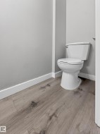 White toilet with a chrome flush handle, set against gray walls with white baseboards and wood-finish flooring - 