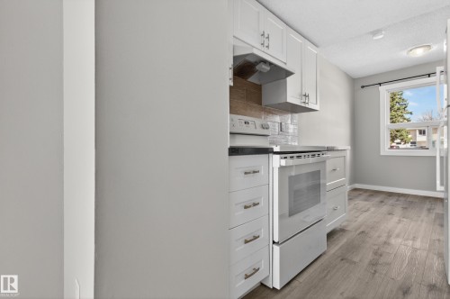 Contemporary kitchen featuring white cabinetry, black countertops, stainless steel appliances, and a tiled backsplash - 18 Lakewood Village, Edmonton, AB - Indoor Photo Showing Kitchen