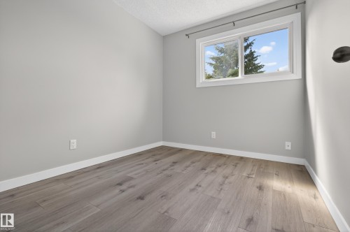 Interior room featuring wood-finish flooring, light grey painted walls, white baseboards, and a window with white trim - 18 Lakewood Village, Edmonton, AB - Indoor Photo Showing Other Room
