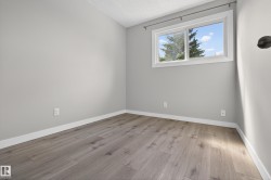 Interior room featuring wood-finish flooring, light grey painted walls, white baseboards, and a window with white trim - 