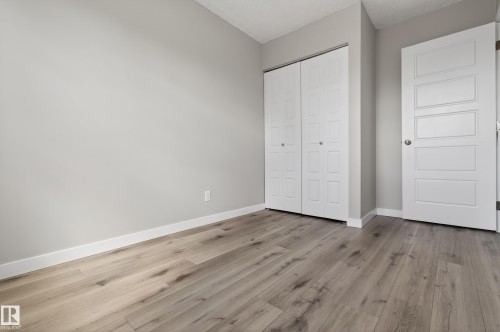 Light wood-finish flooring complements the neutral wall color in this room, featuring a white bi-fold closet door and a paneled interior door with a chrome knob - 18 Lakewood Village, Edmonton, AB - Indoor Photo Showing Other Room