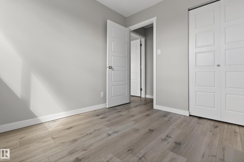 Room featuring wood-finish flooring, light grey painted walls, white trim, and a white paneled door - 18 Lakewood Village, Edmonton, AB - Indoor Photo Showing Other Room