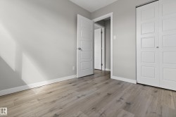 Room featuring wood-finish flooring, light grey painted walls, white trim, and a white paneled door - 