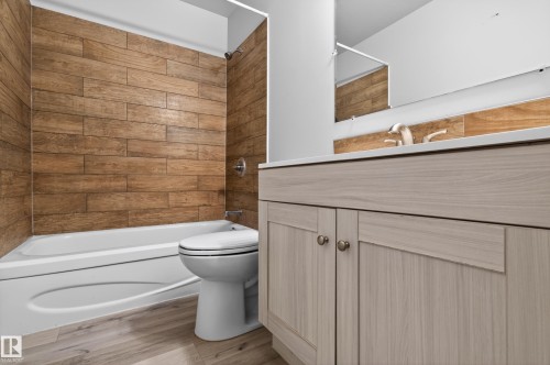 Bathroom featuring a white bathtub with wood-finish tile surround, a light wood-finish vanity, a white countertop, and wood-finish flooring - 18 Lakewood Village, Edmonton, AB - Indoor Photo Showing Bathroom