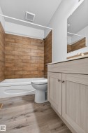 Bathroom featuring a white bathtub, wood-finish wall tile, light wood-finish vanity with cabinet storage, light-toned countertop, and wood-finish flooring - 