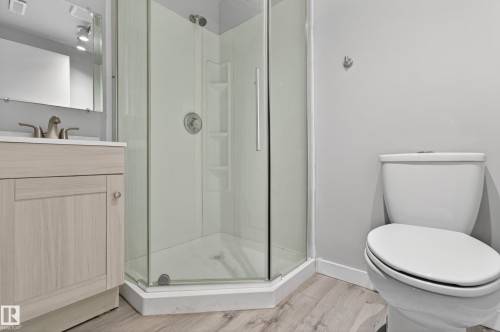 Bathroom featuring a corner glass shower enclosure, a vanity with a light wood-finish cabinet and white countertop, and wood-finish flooring - 18 Lakewood Village, Edmonton, AB - Indoor Photo Showing Bathroom