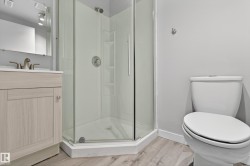 Bathroom featuring a corner glass shower enclosure, a vanity with a light wood-finish cabinet and white countertop, and wood-finish flooring - 