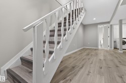 Wood-finish flooring extending from the open space, featuring a staircase with white balusters and wood-finish treads - 
