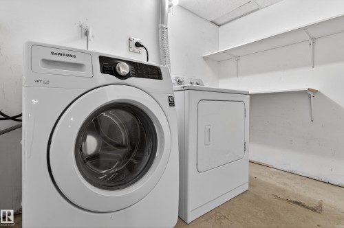 Dedicated utility space featuring a front-load washing machine, a clothes dryer, and wall-mounted shelving for storage - 18 Lakewood Village, Edmonton, AB - Indoor Photo Showing Laundry Room