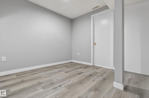 Room featuring wood-finish flooring, light grey walls, white trim, and a white door with brass hardware - 18 Lakewood Village, Edmonton, AB - Indoor Photo Showing Other Room