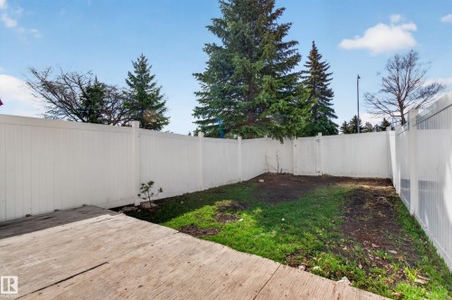 Private backyard featuring white vinyl fencing, a concrete patio area, and mature evergreen trees - 18 Lakewood Village, Edmonton, AB - Outdoor