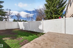 Private rear yard featuring a white panel fence, concrete patio, and a grass area - 