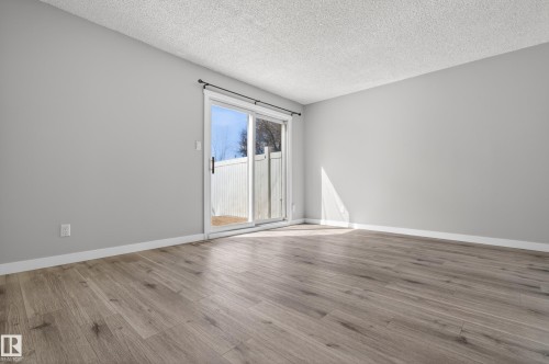 Spacious room featuring wood-finish flooring, light grey painted walls, white baseboards, and a sliding glass door providing access to a private outdoor area with a white fence - 18 Lakewood Village, Edmonton, AB - Indoor Photo Showing Other Room