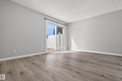 Spacious room featuring wood-finish flooring, light grey painted walls, white baseboards, and a sliding glass door providing access to a private outdoor area with a white fence - 