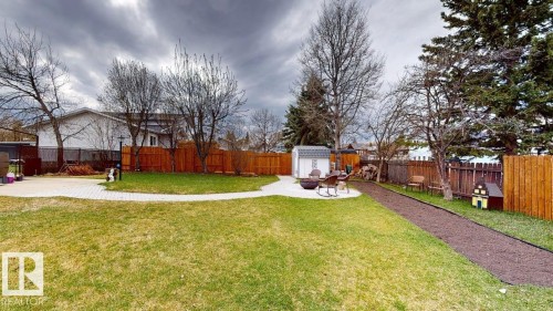 Expansive backyard featuring a lush lawn, a paved patio area, a storage shed, a wood fence, and mature trees - 4116 55C Ave, Drayton Valley, AB - Outdoor