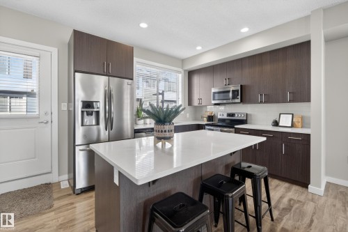 Kitchen featuring a central island with a white countertop, dark wood-finish cabinetry, stainless steel appliances, and wood-finish flooring - 61 2803 James Mowatt Trail, Edmonton, AB - Indoor Photo Showing Kitchen With Stainless Steel Kitchen With Upgraded Kitchen