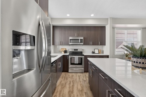 Kitchen featuring stainless steel appliances, dark wood-finish cabinetry, white countertops, wood-finish flooring, and recessed lighting - 61 2803 James Mowatt Trail, Edmonton, AB - Indoor Photo Showing Kitchen With Stainless Steel Kitchen With Upgraded Kitchen