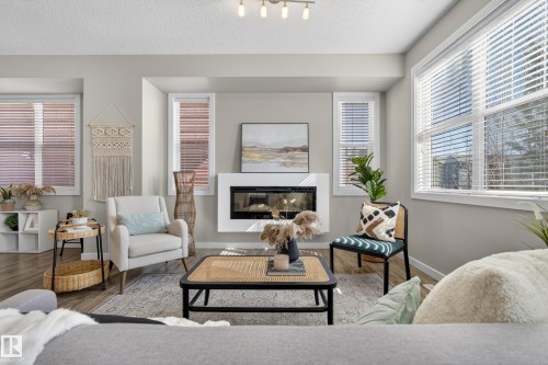 Living area featuring a modern linear fireplace with a white surround, wood-finish flooring, and multiple windows with blinds - 61 2803 James Mowatt Trail, Edmonton, AB - Indoor Photo Showing Living Room With Fireplace