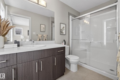 Contemporary bathroom featuring a dark wood-finish vanity with a white countertop and undermount sink, a large wall mirror, a framed glass shower enclosure, and tiled flooring - 61 2803 James Mowatt Trail, Edmonton, AB - Indoor Photo Showing Bathroom