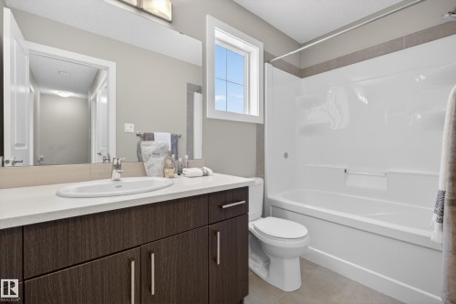 Bathroom featuring an integrated vanity sink with a light-toned countertop, wood-finish cabinetry, a white toilet, and a white bathtub with an integrated shower - 61 2803 James Mowatt Trail, Edmonton, AB - Indoor Photo Showing Bathroom