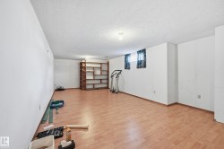 Spacious lower-level room featuring wood-finish flooring, white walls, and built-in shelving - 