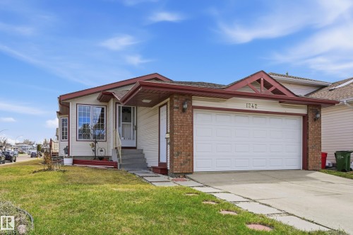 Single-story residence featuring light-colored siding, a two-car garage with white paneling, and a brick facade accent - 1242 Joyce Crescent, Edmonton, AB - Outdoor With Facade