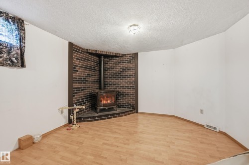 Wood-finish flooring and white walls complement a corner brick-clad wood-burning stove with a matching hearth - 1242 Joyce Crescent, Edmonton, AB - Indoor With Fireplace