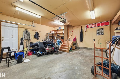 Spacious garage with concrete flooring, fluorescent overhead lighting, an interior access door, built-in shelving, and a wooden staircase - 1242 Joyce Crescent, Edmonton, AB - Indoor Photo Showing Garage