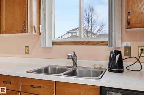 Kitchen area featuring a stainless steel double-basin sink with a chrome faucet, light-toned countertops, and wood cabinetry - 1242 Joyce Crescent, Edmonton, AB - Indoor Photo Showing Kitchen With Double Sink