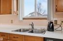 Kitchen area featuring a stainless steel double-basin sink with a chrome faucet, light-toned countertops, and wood cabinetry - 1242 Joyce Crescent, Edmonton, AB  - Indoor Photo Showing Kitchen With Double Sink 