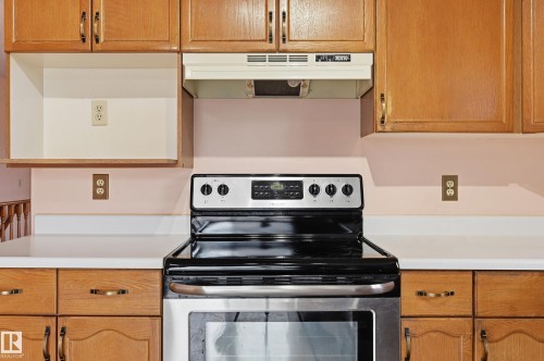 Kitchen featuring a stainless steel electric range, warm wood cabinetry with bronze hardware, white countertops, and a white range hood - 1242 Joyce Crescent, Edmonton, AB - Indoor Photo Showing Kitchen