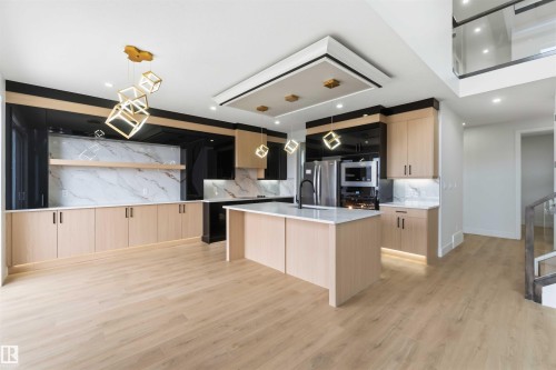 Modern kitchen featuring a central island with a light-toned countertop, wood-finish cabinetry, integrated stainless steel appliances, a marble-look backsplash, and unique geometric pendant lighting - 417 Pine Point(E), Leduc, AB - Indoor Photo Showing Kitchen With Upgraded Kitchen