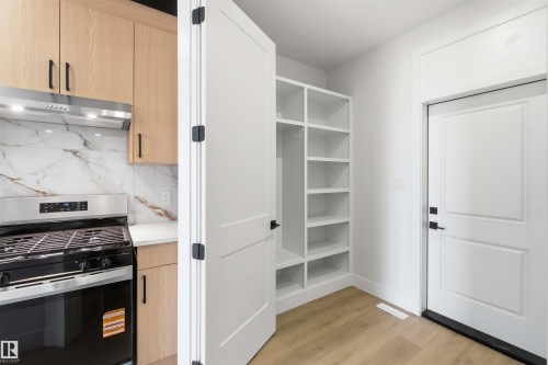Kitchen area featuring a stainless steel range with overhead ventilation, light wood-finish cabinetry, and a white countertop - 417 Pine Point(E), Leduc, AB - Indoor