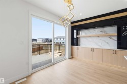 Spacious room featuring light wood-finish flooring, a wall of built-in cabinetry with a white countertop and marble-patterned backsplash, and a modern geometric light fixture - 