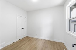 Light wood-finish flooring complements crisp white walls in this room, featuring a double-door closet with matte black hardware and a large window providing natural illumination - 