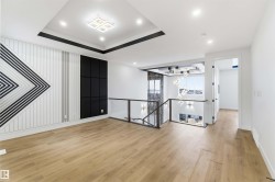 Open-concept living space featuring wood-finish flooring, a tiered ceiling with recessed lighting and a central fixture, and a decorative wall with geometric paneling - 